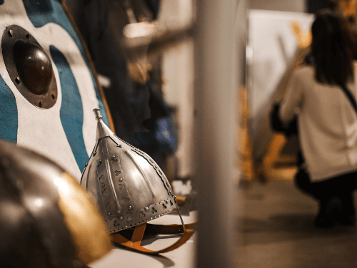 A viking hat sat on a bench resting on a round shield.