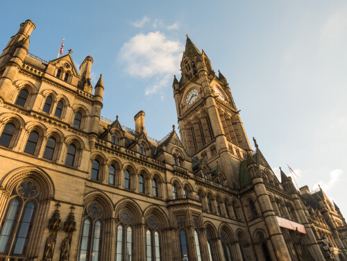 manchester city hall from below, the sky is clear in the background and the sun shines softly onto the gothic building.