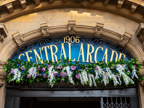 The sign of Newcastle's central arcade perched above a doorway with flowers beneath the sign.